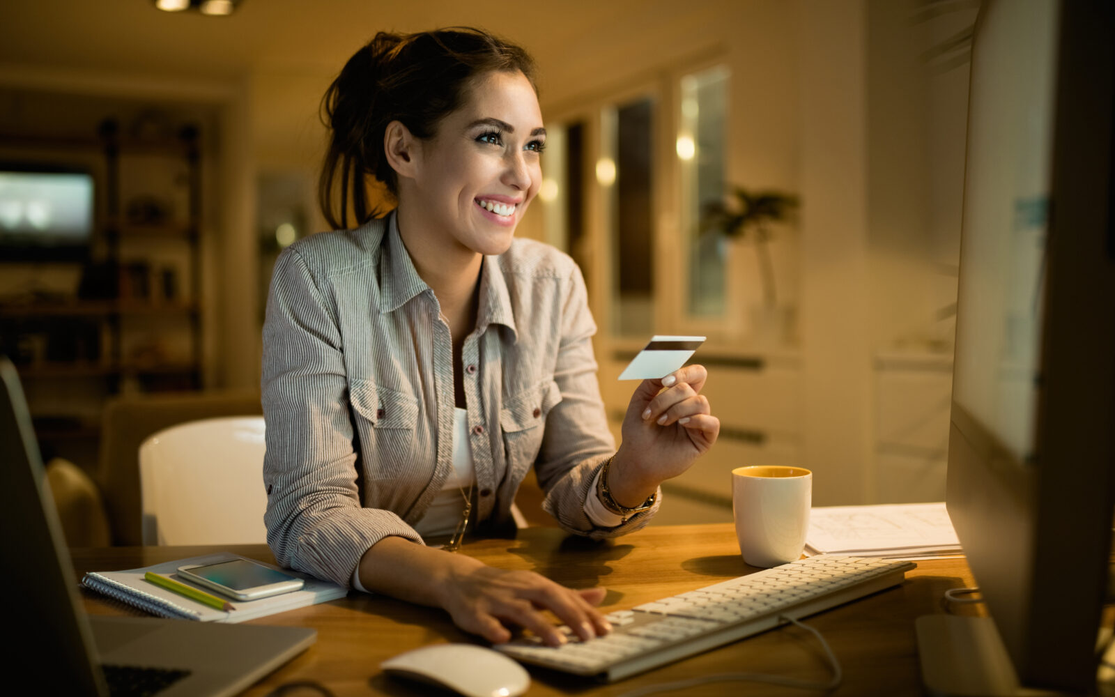 Happy woman using credit card for online banking at night at hom